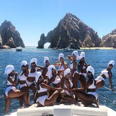 a group of women in bathing suits sitting on the back of a boat with rocks in the background