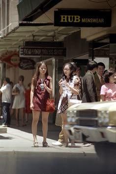 two girls are walking down the street in front of some cars and people with umbrellas