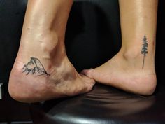 two people with tattoos on their feet standing next to each other, one has a mountain and the other is a pine tree