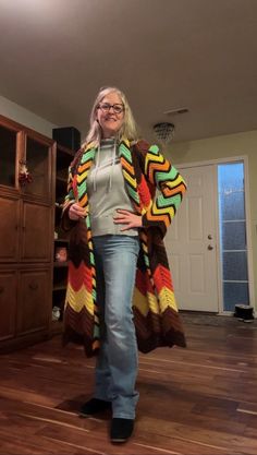 a woman standing in a living room wearing a multicolored cardigan sweater and jeans