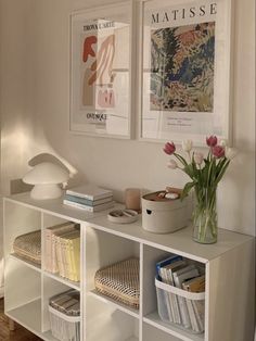 a white shelf with some books and flowers on it next to a vase filled with tulips