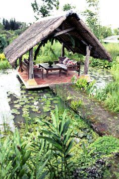 a wooden gazebo sitting on top of a lush green field next to a pond