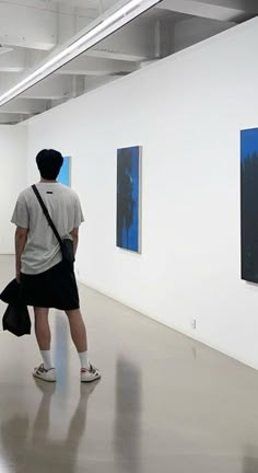 two people standing in an art gallery looking at paintings on the wall and one person holding a bag