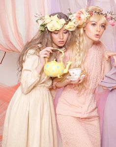 two beautiful young women standing next to each other holding cups and teapots in their hands