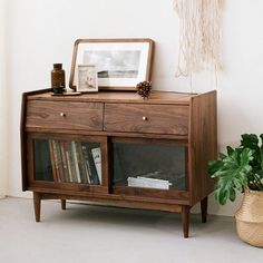 a wooden cabinet sitting next to a potted plant on top of a white floor