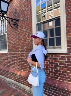 a woman standing in front of a brick building with a white purse on her hip