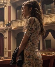 a woman standing in front of a stage wearing a floral dress and carrying a purse