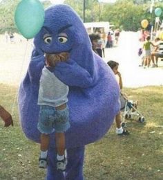 a child standing next to an inflatable blue monster holding a green ballon