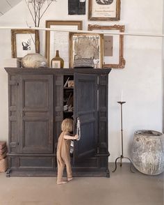 a young child reaching into an old wooden cabinet in a room with pictures on the wall