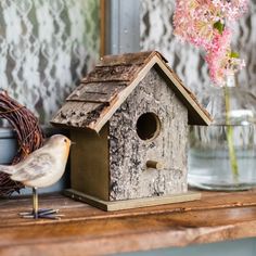 a birdhouse sitting on top of a wooden table next to a vase with flowers