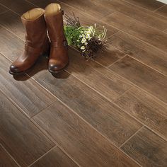 a pair of brown boots sitting on top of a wooden floor next to a plant