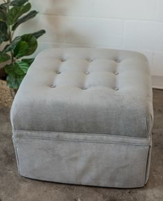 a grey ottoman sitting on top of a floor next to a potted plant