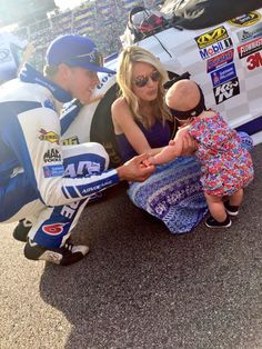 a woman holding a baby in front of a race car