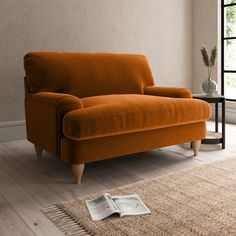 an orange couch sitting on top of a wooden floor next to a rug and window