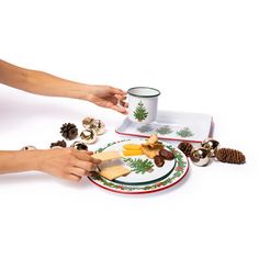 two hands reaching for food on a plate with pine cones and christmas decorations around it