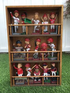 a wooden shelf filled with baseball figurines on top of grass