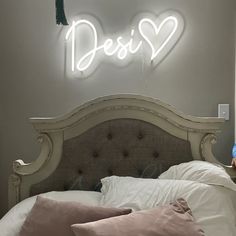 a person sitting on a bed in front of a neon sign that says dessi