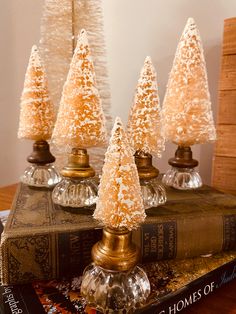 four small white trees sitting on top of a table next to an old book and lamp