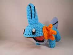 a crocheted blue toy with an orange flower in it's mouth, on a white background