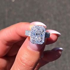 a woman's hand holding an engagement ring with a diamond in the center and two rows of diamonds on each side