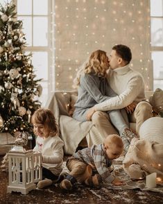 a man and woman are sitting on a couch with their children in front of a christmas tree