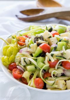 a salad with cucumbers, tomatoes and other vegetables in a bowl next to a wooden spoon