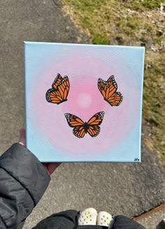 a person holding up a painting with three orange butterflies on it's face in the air