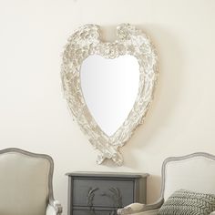 a heart shaped mirror hanging on the wall above two chairs and a dresser in a living room