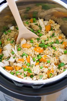 a crock pot filled with rice, peas and carrots next to a wooden spoon