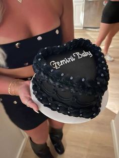 a woman holding a black heart shaped cake