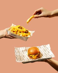 two hands reaching for a hamburger with macaroni and cheese on it, while another hand reaches out to grab one