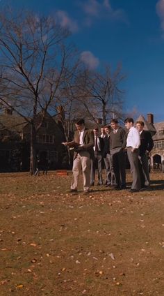 a group of men standing next to each other in front of a building on a field