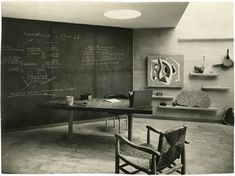 a black and white photo of a room with chalk writing on the wall, two chairs in front of a table