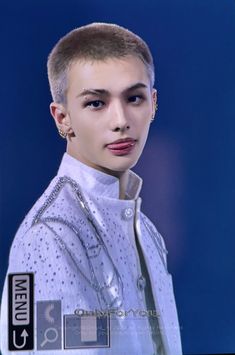 a young man with short hair and piercings on his head wearing a white jacket