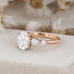 a rose gold engagement ring with three diamonds on it and flowers in the back ground