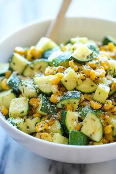 a white bowl filled with zucchini and corn salad on top of a marble counter