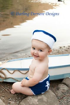 a baby sitting on the ground next to a small boat and smiling at the camera