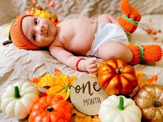 a baby laying on top of a bed surrounded by pumpkins and other fall decorations