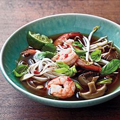 a green bowl filled with shrimp, noodles and veggies on top of a wooden table