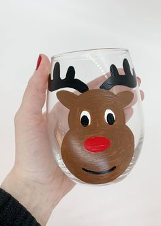 a hand holding up a wine glass with a reindeer face painted on the side and nose