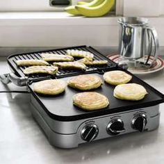 an electric griddle grill with six pancakes cooking on it and bananas in the background