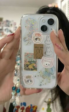 a woman holding up her phone case with stickers on it and some beads hanging from the back