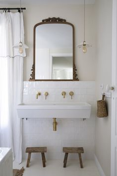 a bathroom with a white sink and wooden stools in front of a large mirror