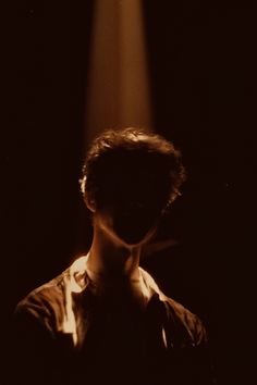 a man standing in the dark with his head turned to the side and light coming from behind him