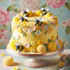 a yellow cake decorated with flowers and bees on a table next to other decorations,