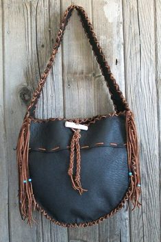 a black purse hanging on the side of a wooden wall with beads and tassels