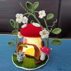 a crocheted mushroom house with flowers and mushrooms on the roof is sitting on a blue surface