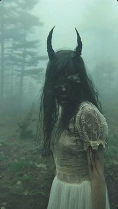 a woman with horns on her head standing in the woods