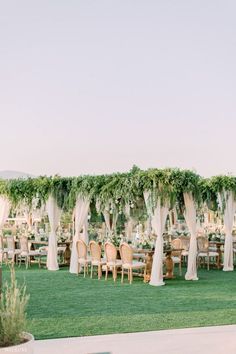 an outdoor wedding setup with white drapes and greenery on the walls, tables and chairs