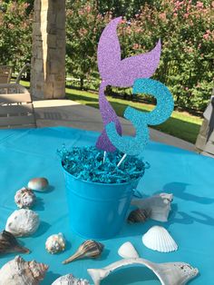 a blue bucket filled with sea shells and a purple cake topper that says 3